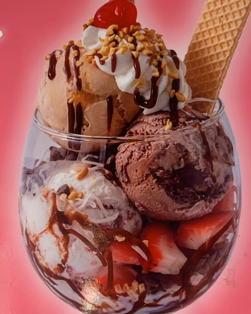 Copa de helado con frutas, crema, maní, cereza, barquillo y galleta sobre fondo rosado.