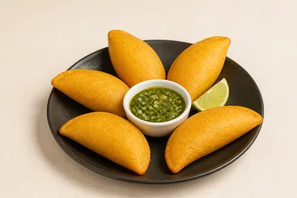Cinco empanadas colombianas de maíz amarillo servidas con ají verde y limón sobre un plato oscuro.