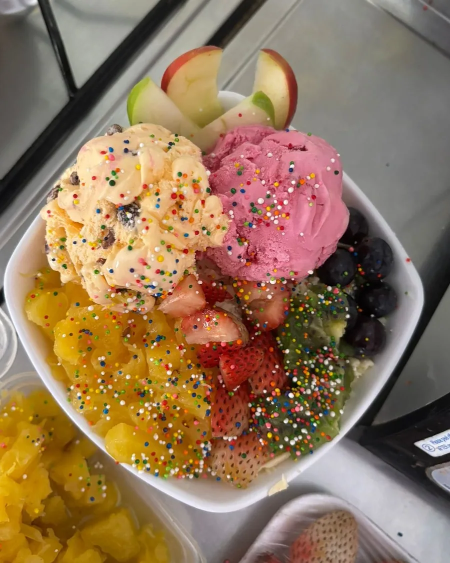 Ensalada de frutas con dos bolas de helado, manzana, fresas, uvas y chispas de colores.