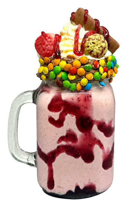 Malteada rosada con crema, galletas, dulces de colores y salsa roja en una jarra de vidrio.