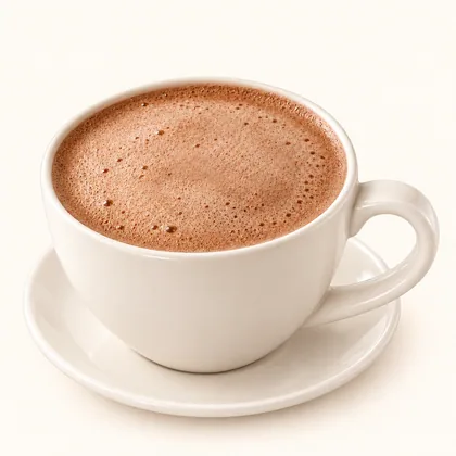 Milo caliente con espuma fina servido en taza crema sobre un plato pequeño.