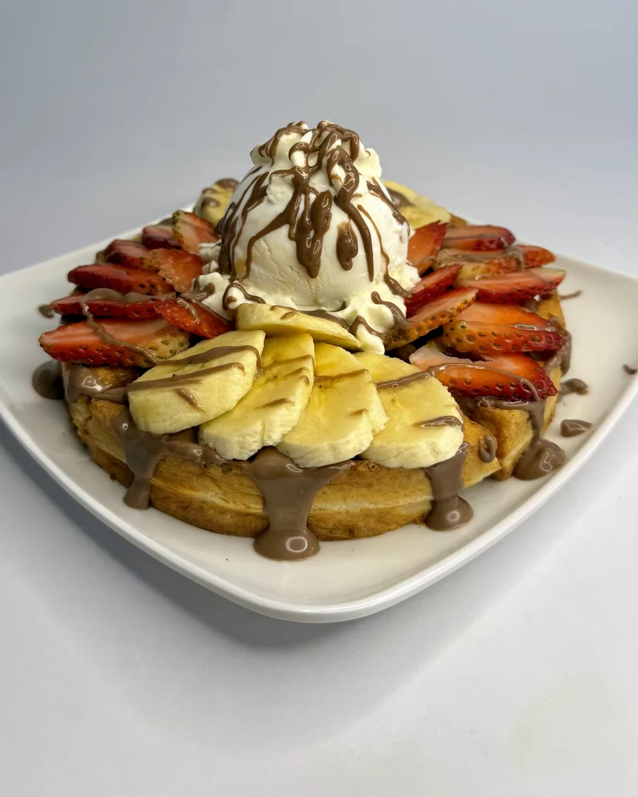 Waffle con banano, fresas, helado, crema y salsa de chocolate.